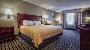 A hotel room with a large bed, two bedside tables, a desk with a chair, a TV, and a window with curtains.