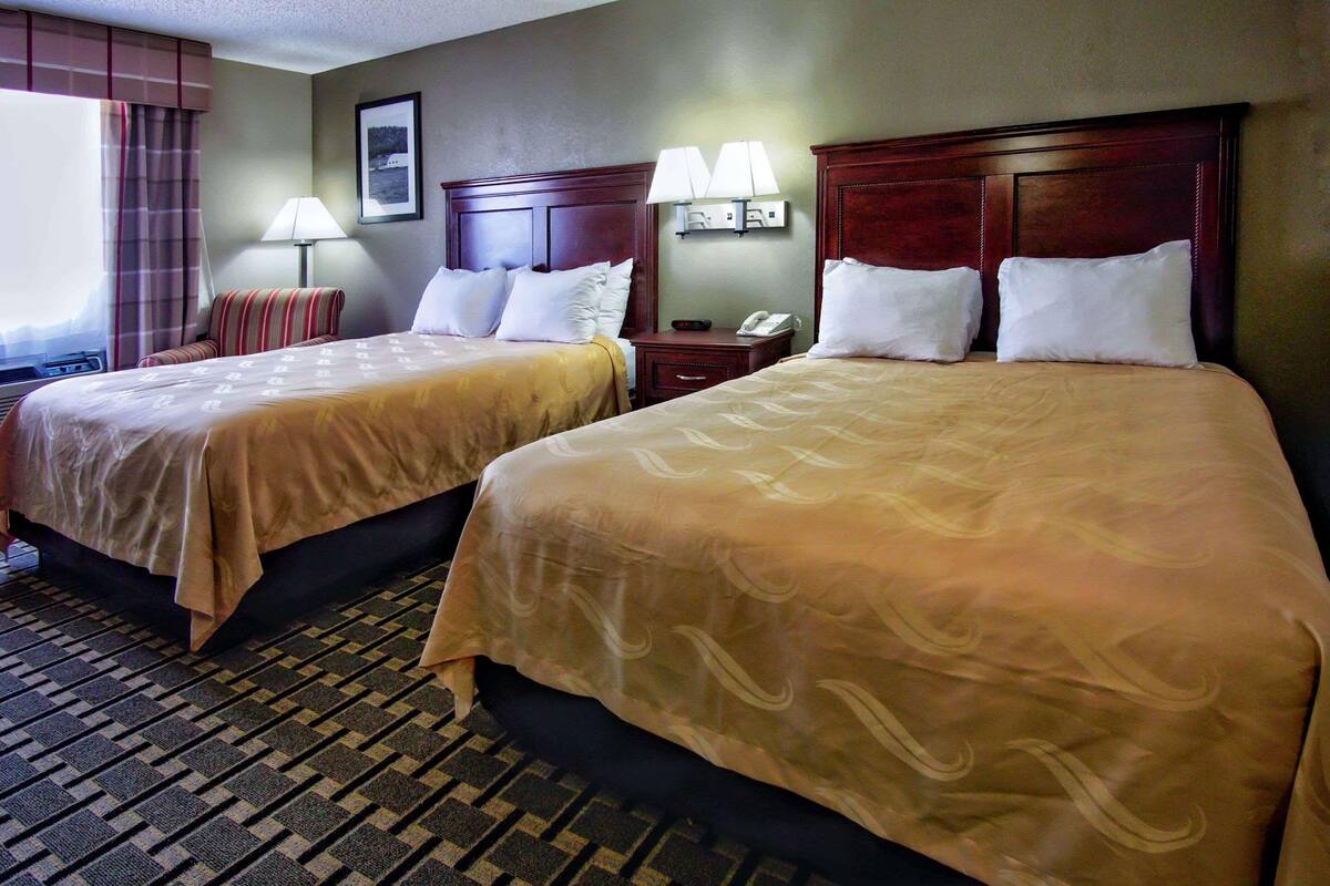A hotel room with two beds, a nightstand, a lamp, a framed picture on the wall, and a window with curtains.