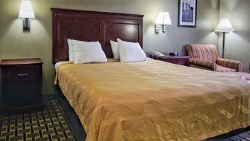 Una habitación de hotel con una cama grande, dos lámparas de noche, una mesita de noche, una silla y un cuadro en la pared.