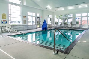 An indoor swimming pool with clear water, safety railings, and white lounge chairs.