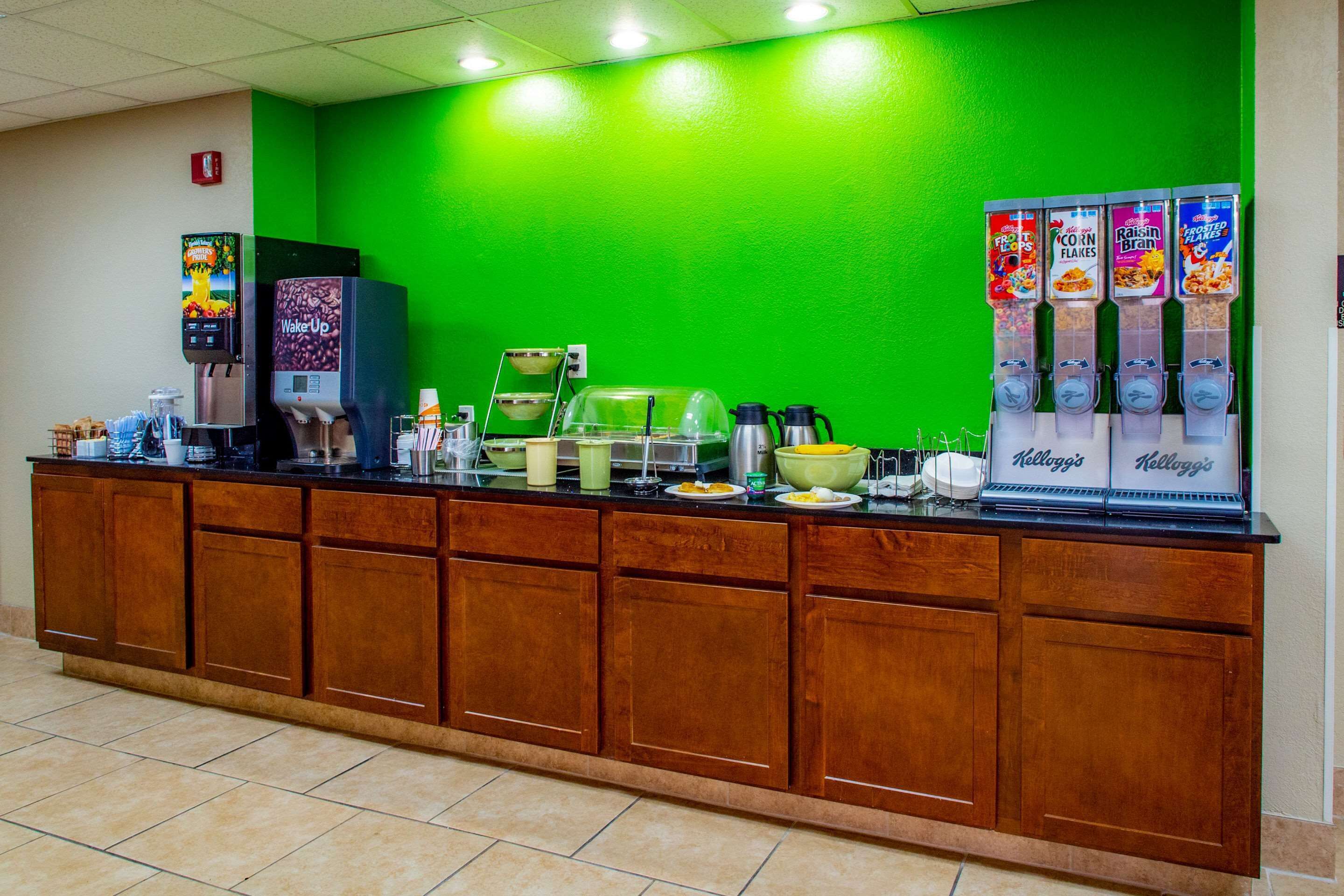 A breakfast bar with a green wall, coffee machines, and cereal dispensers.