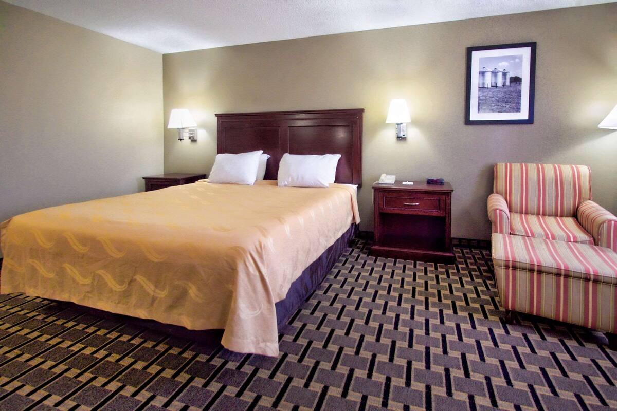 A hotel room with a large bed, two bedside lamps, a chair, and a framed picture on the wall.