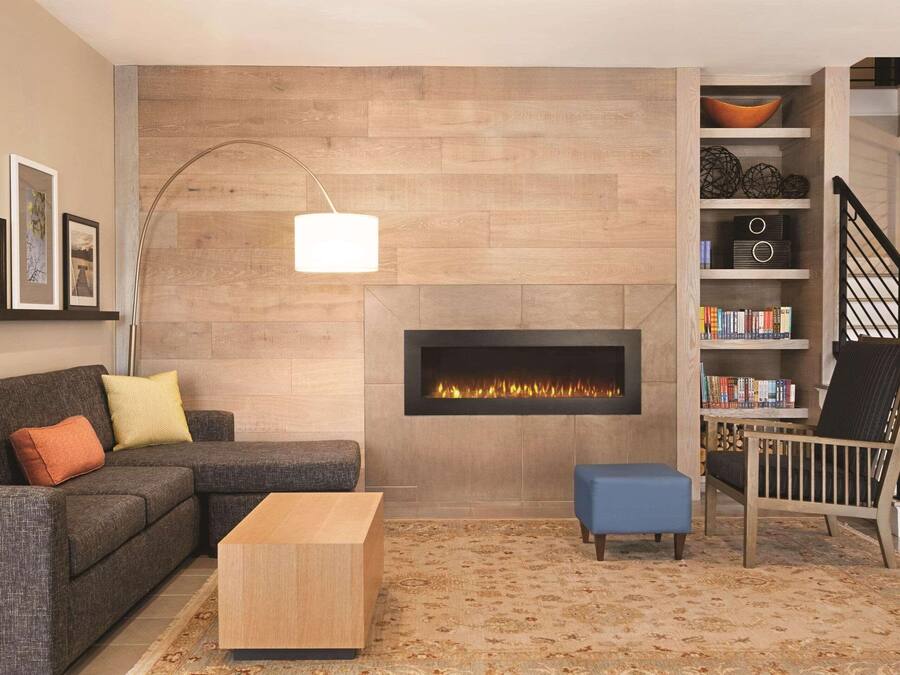 A modern living room with a fireplace, a sofa, a coffee table, a bookshelf, and a staircase.