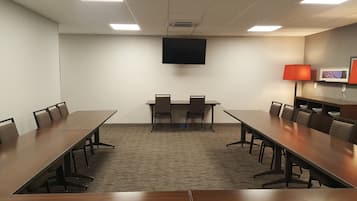 A conference room with a long table, chairs, a flat-screen TV, and a lamp.