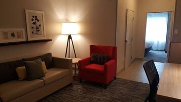 Habitación de hotel con sofá, un sillón rojo, una lámpara de pie y cama con vistas al exterior.