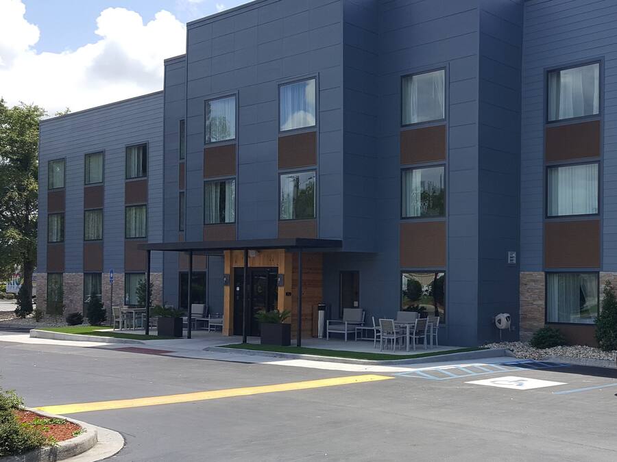A modern multi-story hotel with a flat roof, large windows, and a covered entrance area with outdoor seating.