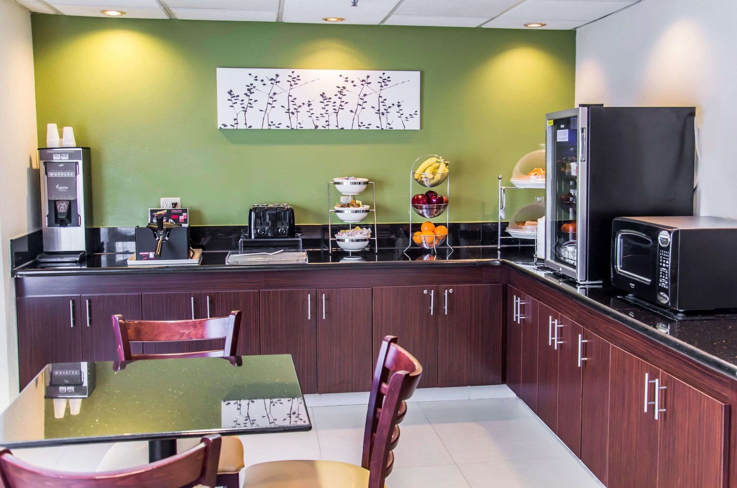A modern kitchen with dark wood cabinets, a black countertop, a microwave, a coffee machine, and a fruit bowl.