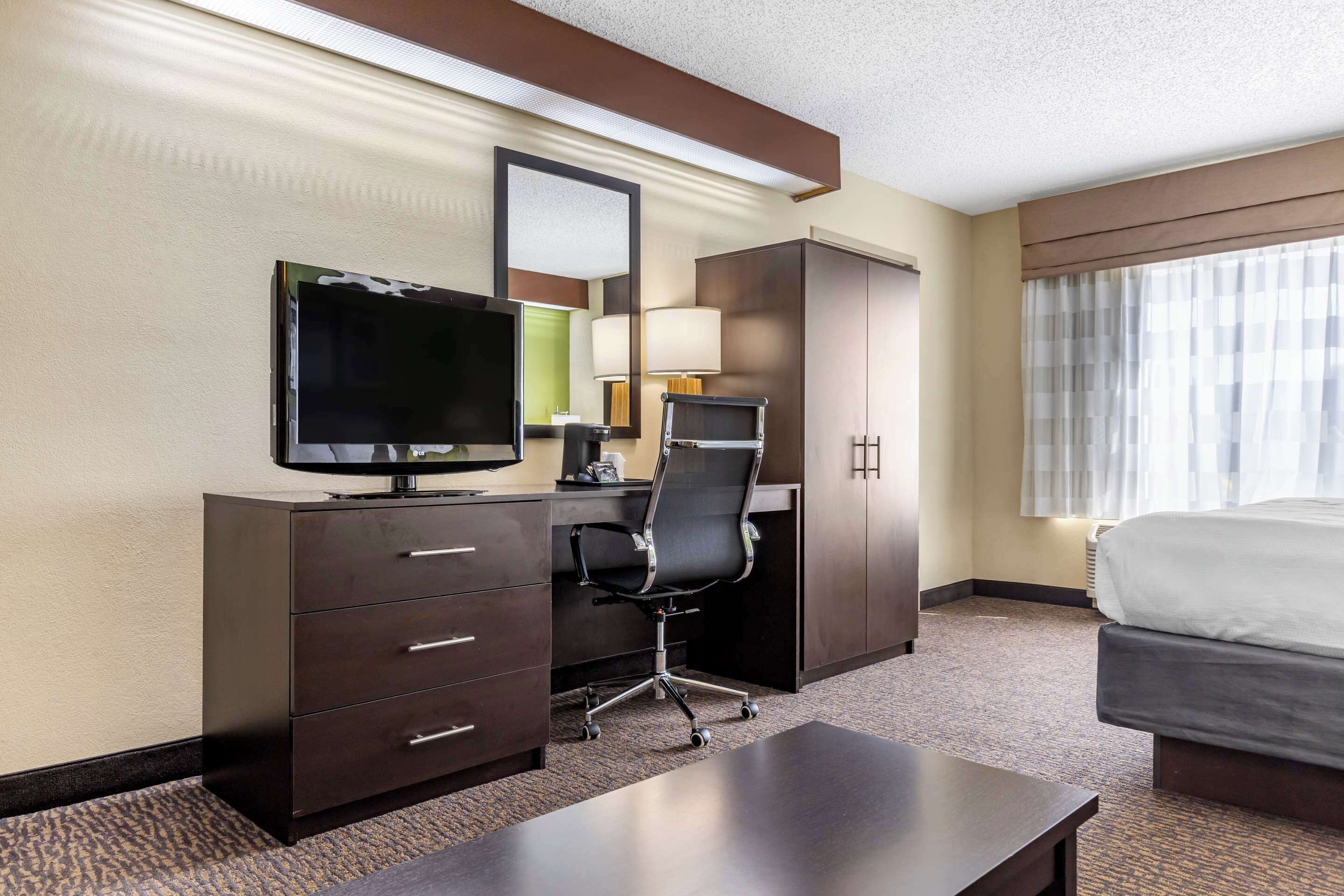 Une chambre d’hôtel comprenant un lit, un bureau avec une télévision, une chaise, une lampe et une armoire.