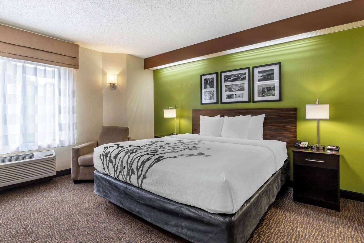 Ein Hotelzimmer mit einem großen Bett, einem Sessel, einem Nachttisch mit Lampe und einer Wand mit gerahmten Bildern.