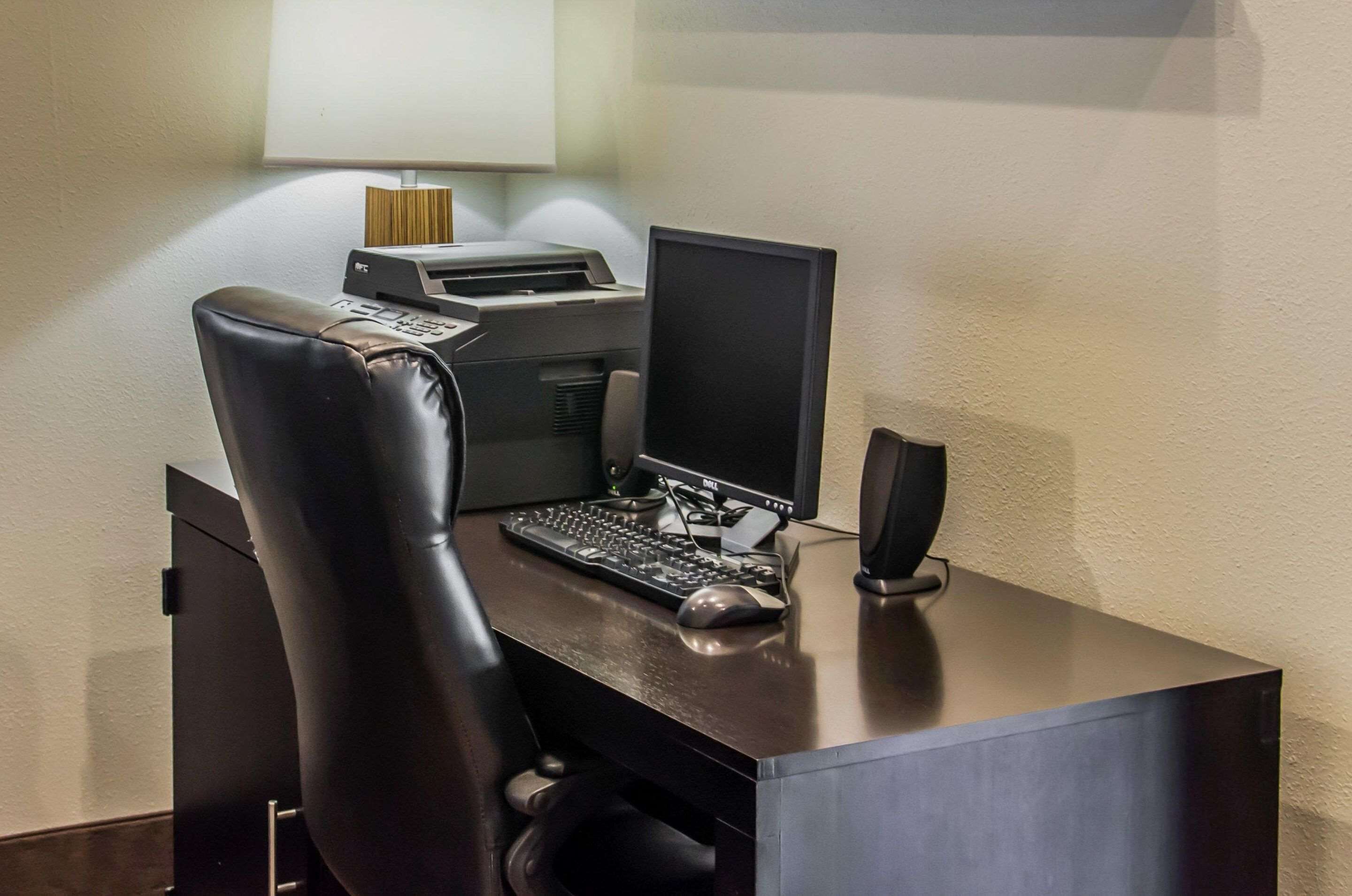 A hotel office with a desk, computer, printer, and chair.