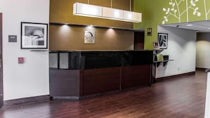 A reception area with a dark reception desk, a sign for 'Sleep Inn', a fire alarm, and a wall with a plant design. - Sleep Inn Matthews - Charlotte (Matthews)