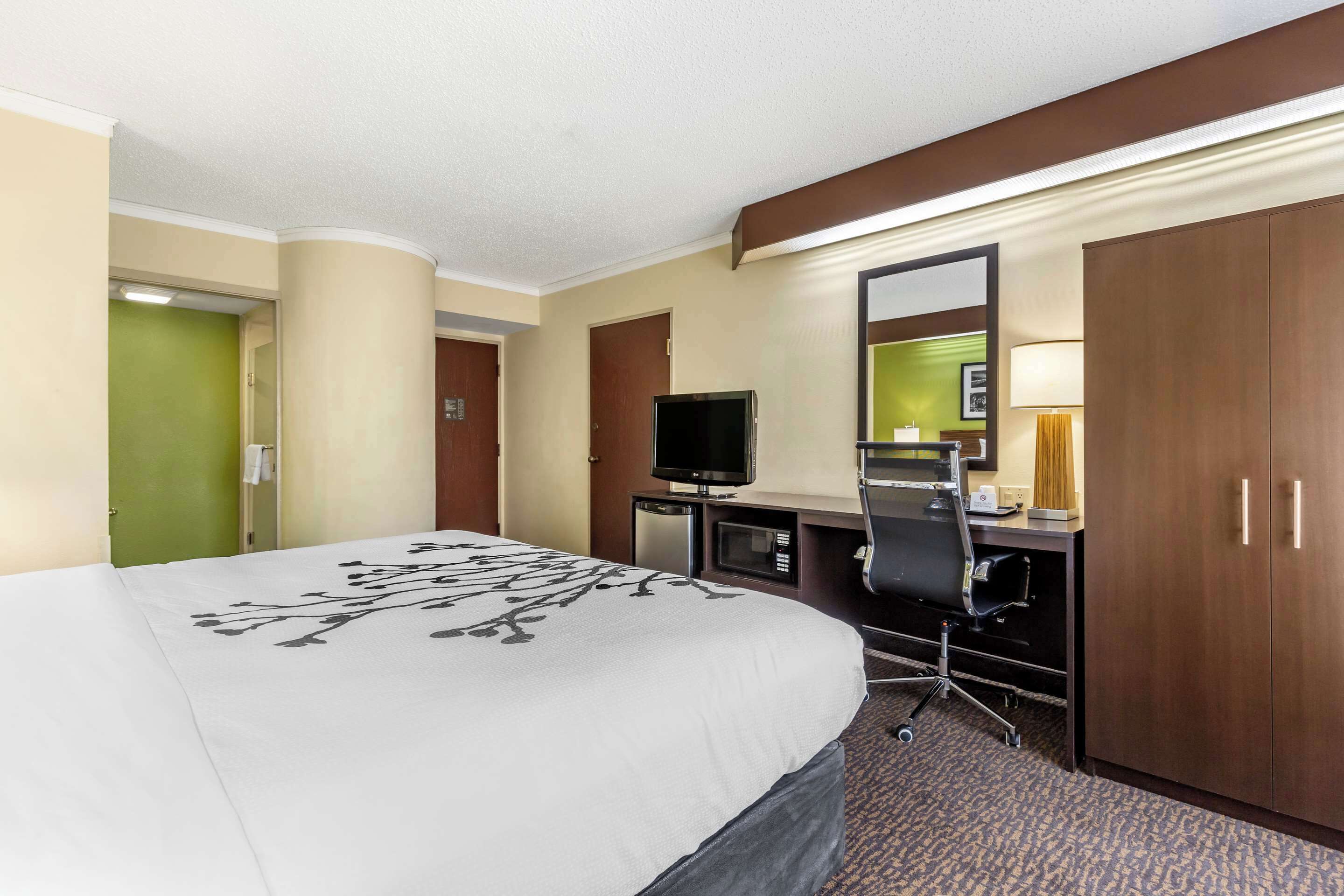 Une chambre d’hôtel avec un grand lit, un bureau avec un ordinateur, une télévision et une armoire.