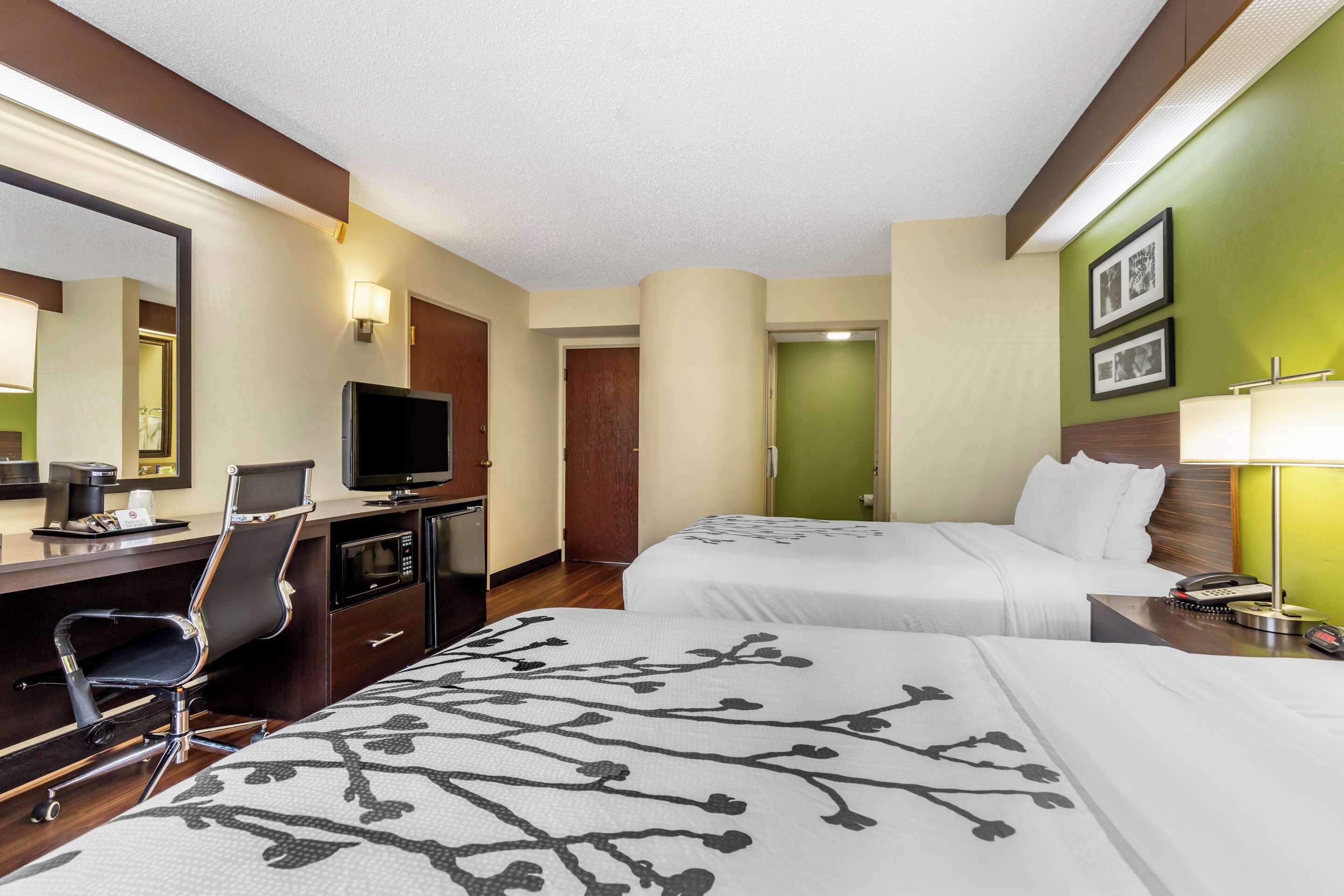 A hotel room with two beds, a desk with a chair, a television, a desk lamp, and a telephone.
