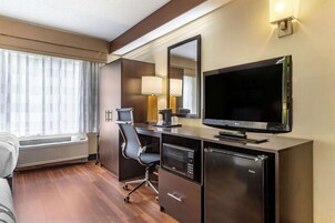 Habitación de hotel con televisor de pantalla plana, escritorio con ordenador, silla, calefactor y refrigerador pequeño.
