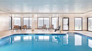 An indoor swimming pool with clear water, surrounded by tiled walls and a wooden floor. There are chairs and a table near the pool, and large windows allow natural light to enter. - Courtyard by Marriott Florence (Florence)