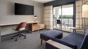 A hotel room with a flat-screen TV, a desk with a chair, a sofa, a small table, and a balcony with outdoor seating. - Courtyard by Marriott Florence (Florence)