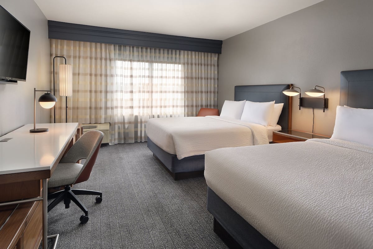 Quarto de hotel com duas camas, uma escrivaninha, uma cadeira e uma televisão.
