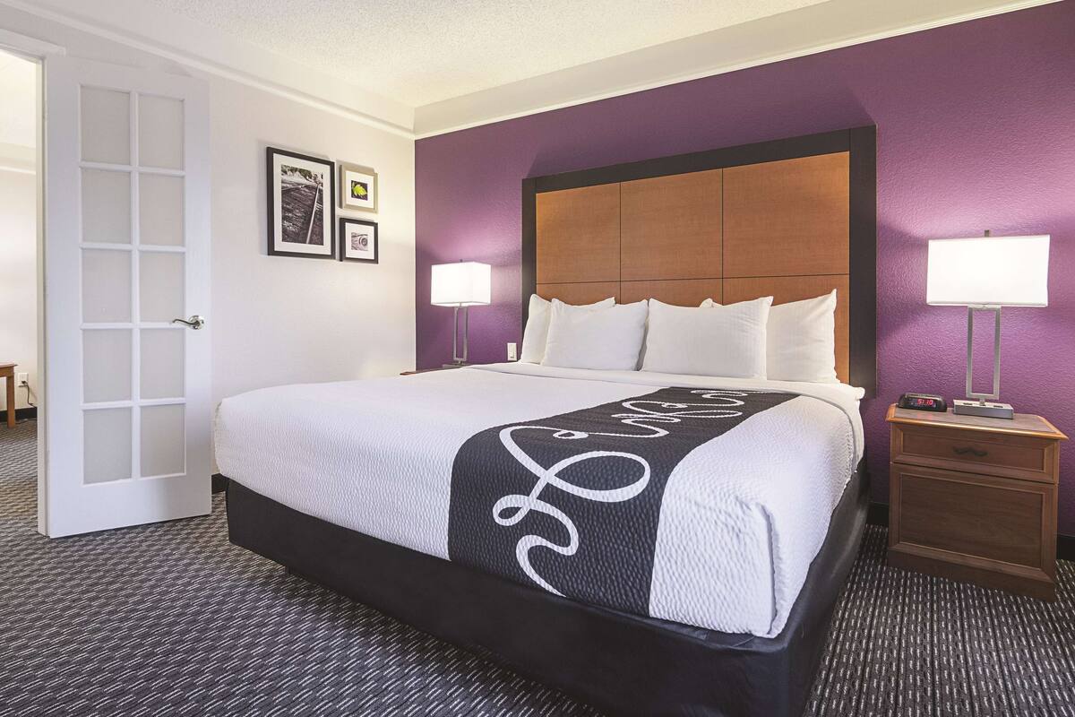 Habitación de hotel con una cama grande, dos lámparas de noche, una mesita de noche de madera y una puerta con paneles de vidrio esmerilado.