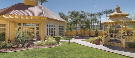 A yellow building with a tiled roof, a covered patio area, and a small gazebo.