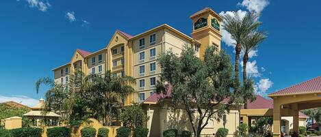 A multi-story hotel with a central clock tower, surrounded by landscaped gardens and palm trees.