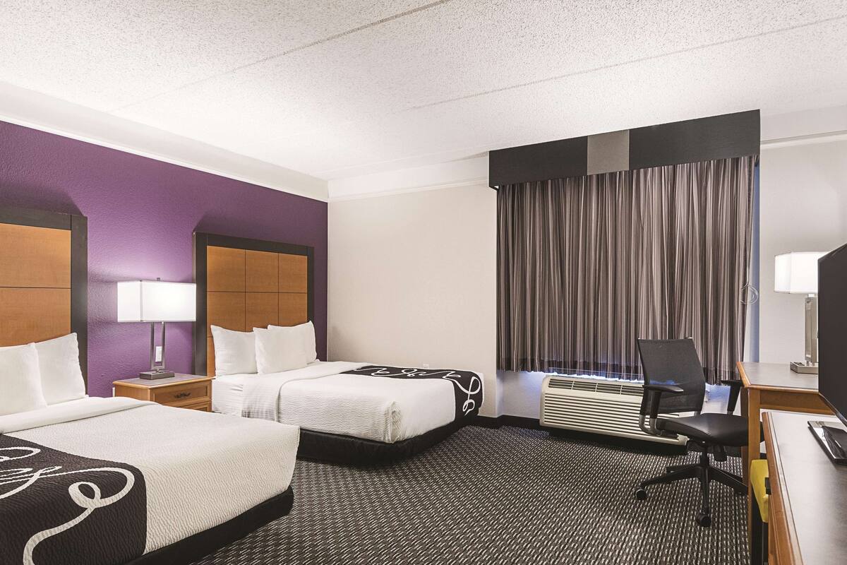 Una habitación de hotel con dos camas, un escritorio, una silla, una lámpara y un equipo de aire acondicionado.