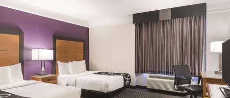 A hotel room with two beds, a desk, a chair, a lamp, and an air conditioning unit.