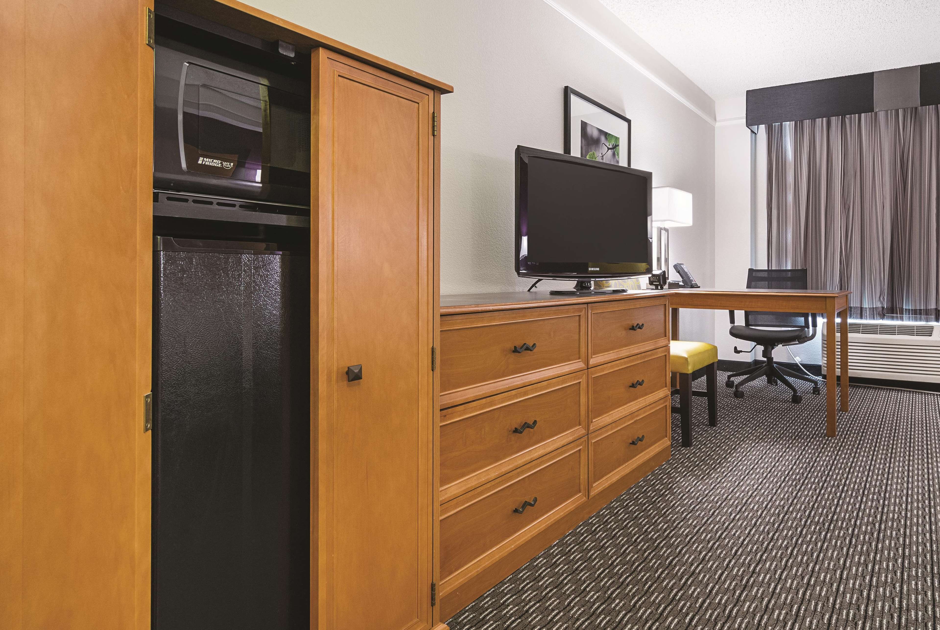 A hotel room with a wooden desk, a television, a chair, and a wardrobe.