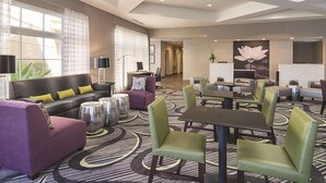 Un hall d’hôtel avec un canapé en cuir noir, des fauteuils violets et un coin repas comprenant des chaises vertes et une table.