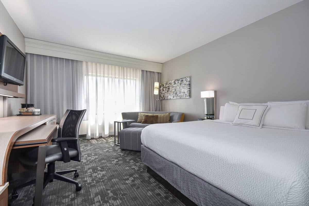A hotel room with a large bed, a desk with a chair, a television, and a window with curtains.