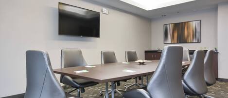 A conference room with a long table, six chairs, a flat-screen TV, and a painting on the wall.