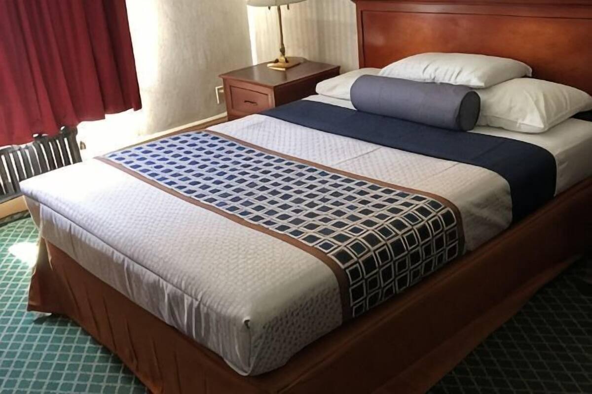 A hotel room with a wooden bed, a nightstand, a lamp, and a window with curtains.