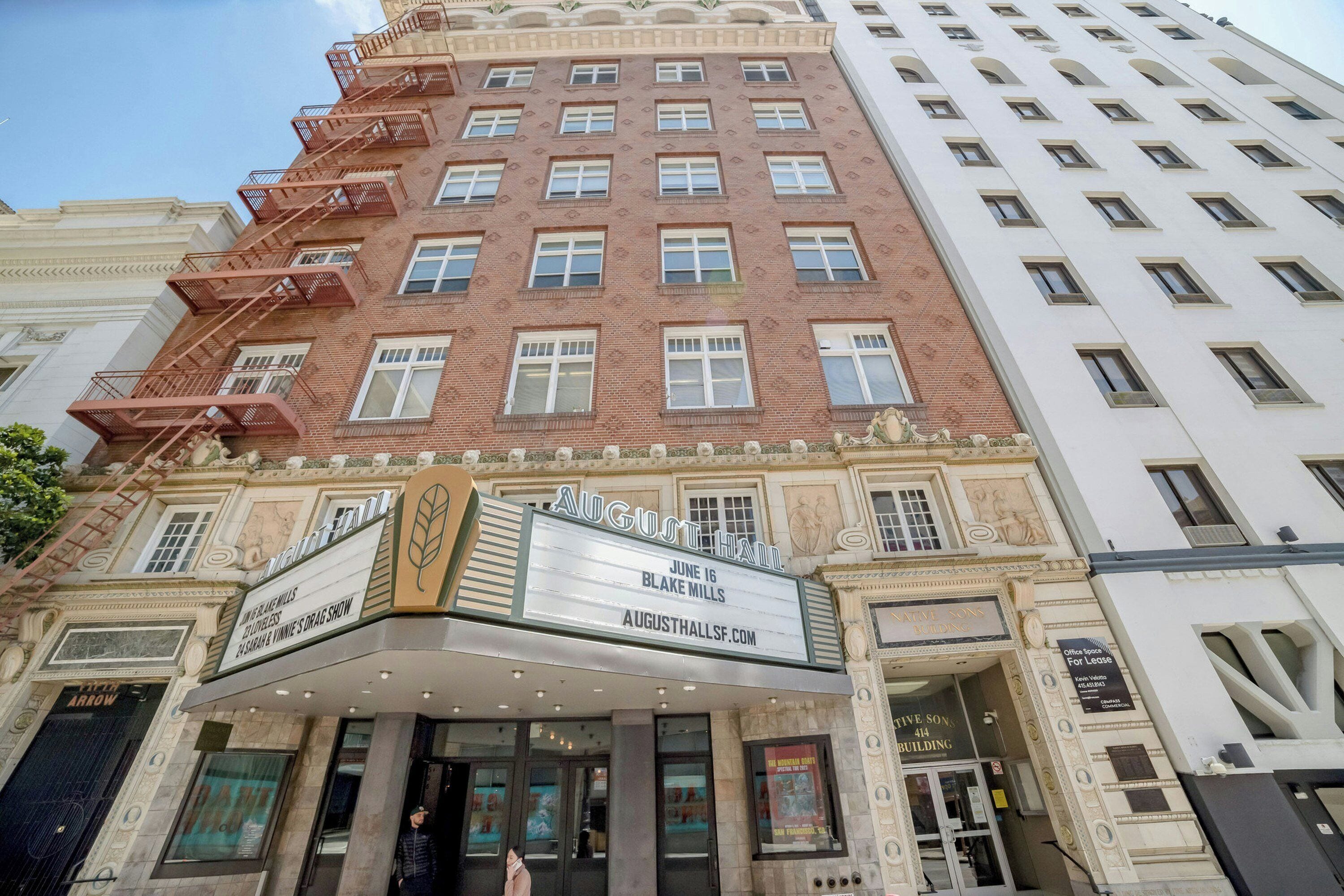 A theater with a marquee advertising a show, a fire escape, and a building with a white facade.
