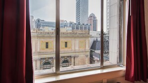 A view from a window with red curtains, overlooking a cityscape with historic buildings and a modern skyscraper. - Union Square Plaza Hotel (San Francisco)