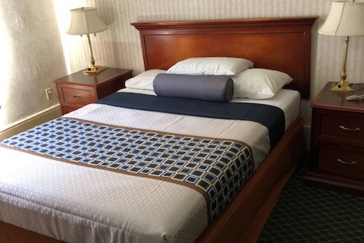 A neatly made bed with a patterned bedspread, a wooden headboard, and two bedside tables with lamps.