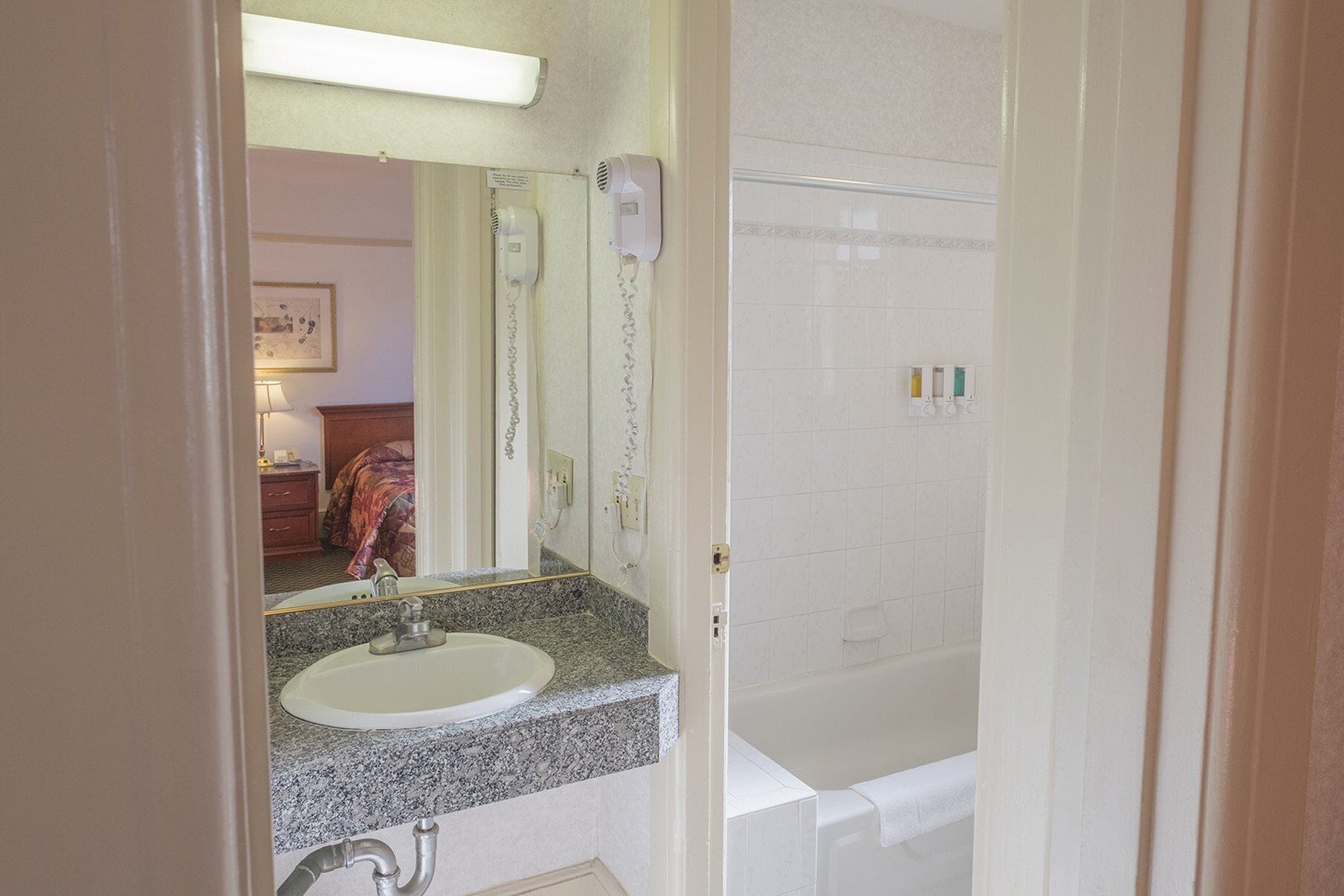 A bathroom with a sink, mirror, hairdryer, and a shower area.