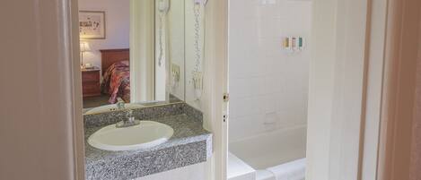 A bathroom with a sink, mirror, hairdryer, and a shower area.