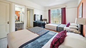 A hotel room with two beds, a TV, a desk with a computer, a bathroom with a sink, and a view of buildings. - Union Square Plaza Hotel (San Francisco)