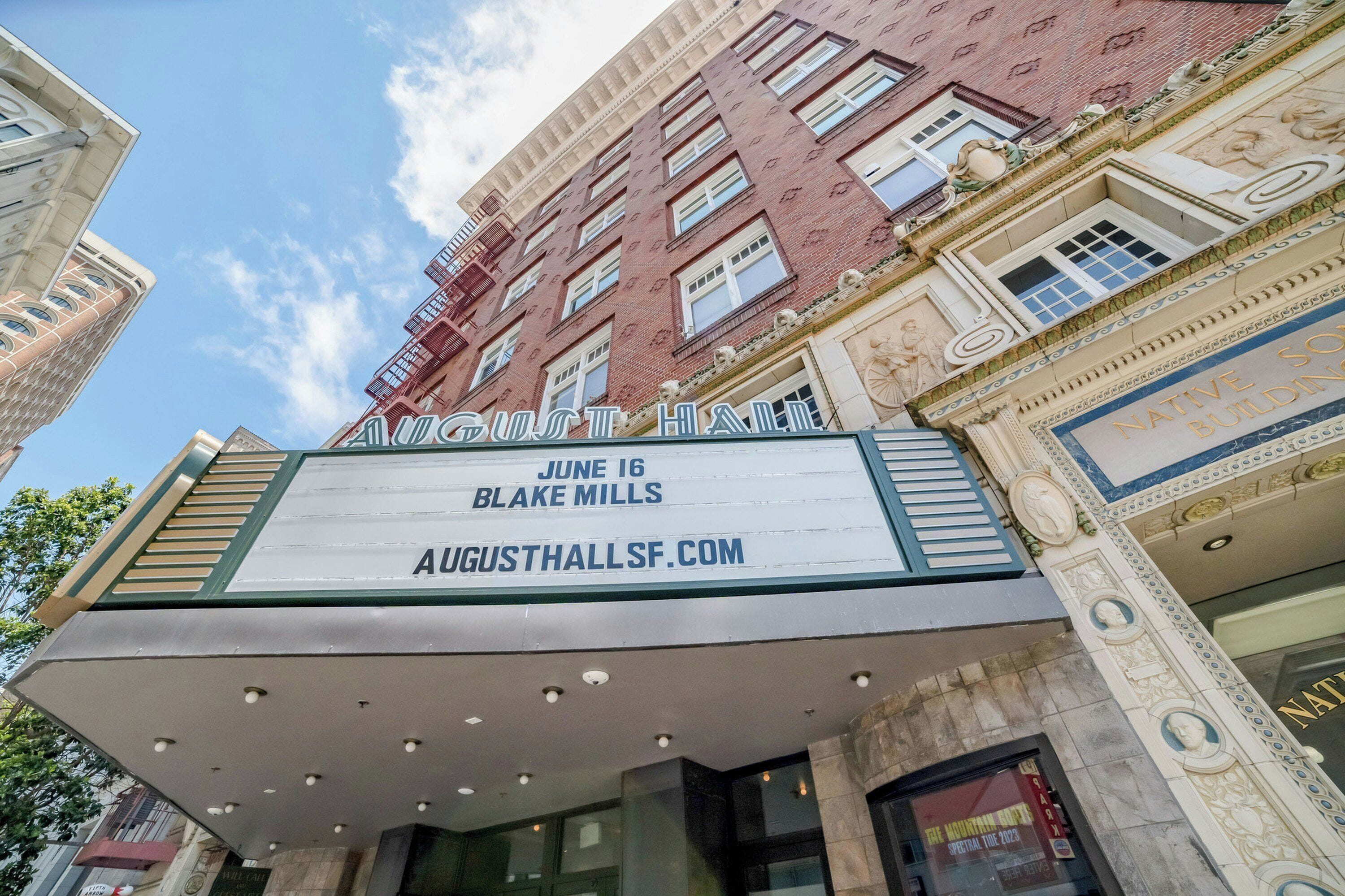A theater marquee with 'August Hall' and 'June 16 Blake Mills' displayed.