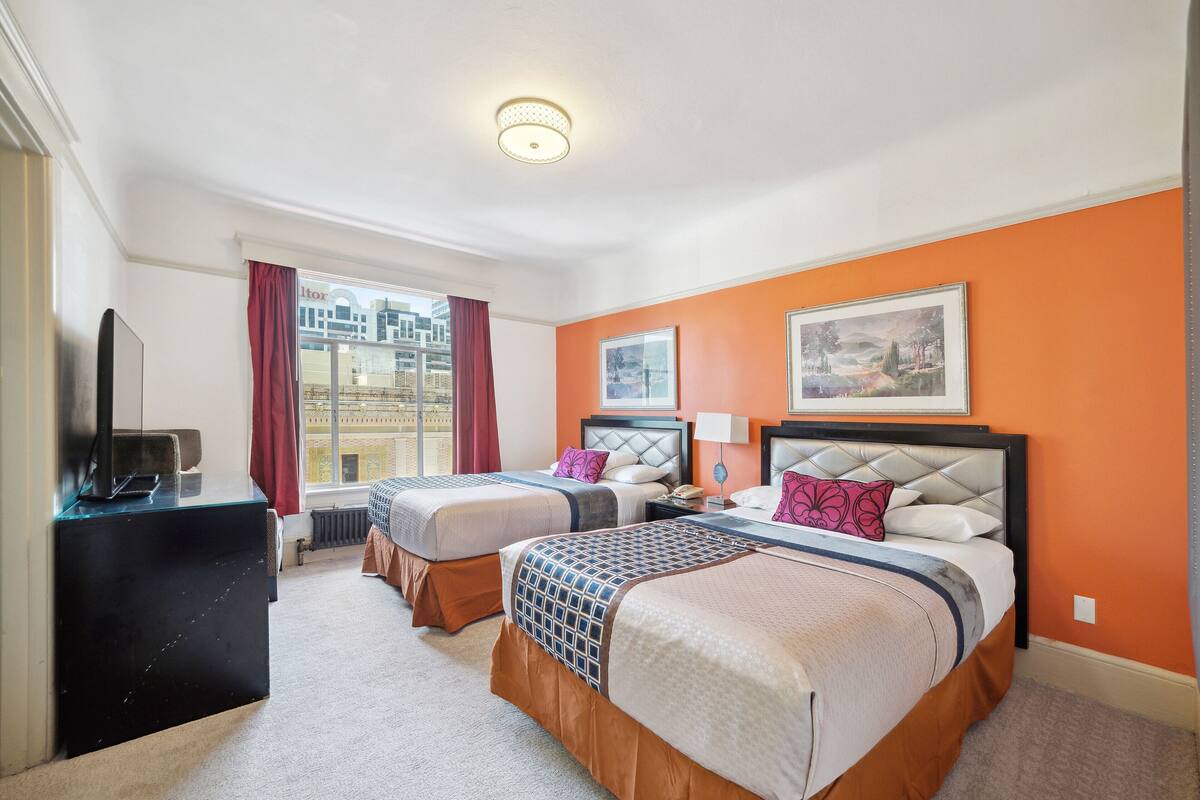 A hotel room with two beds, a TV, and a window with curtains.