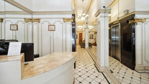 A hotel reception area with a marble counter, framed certificates on the wall, and a tiled floor. - Union Square Plaza Hotel (San Francisco)