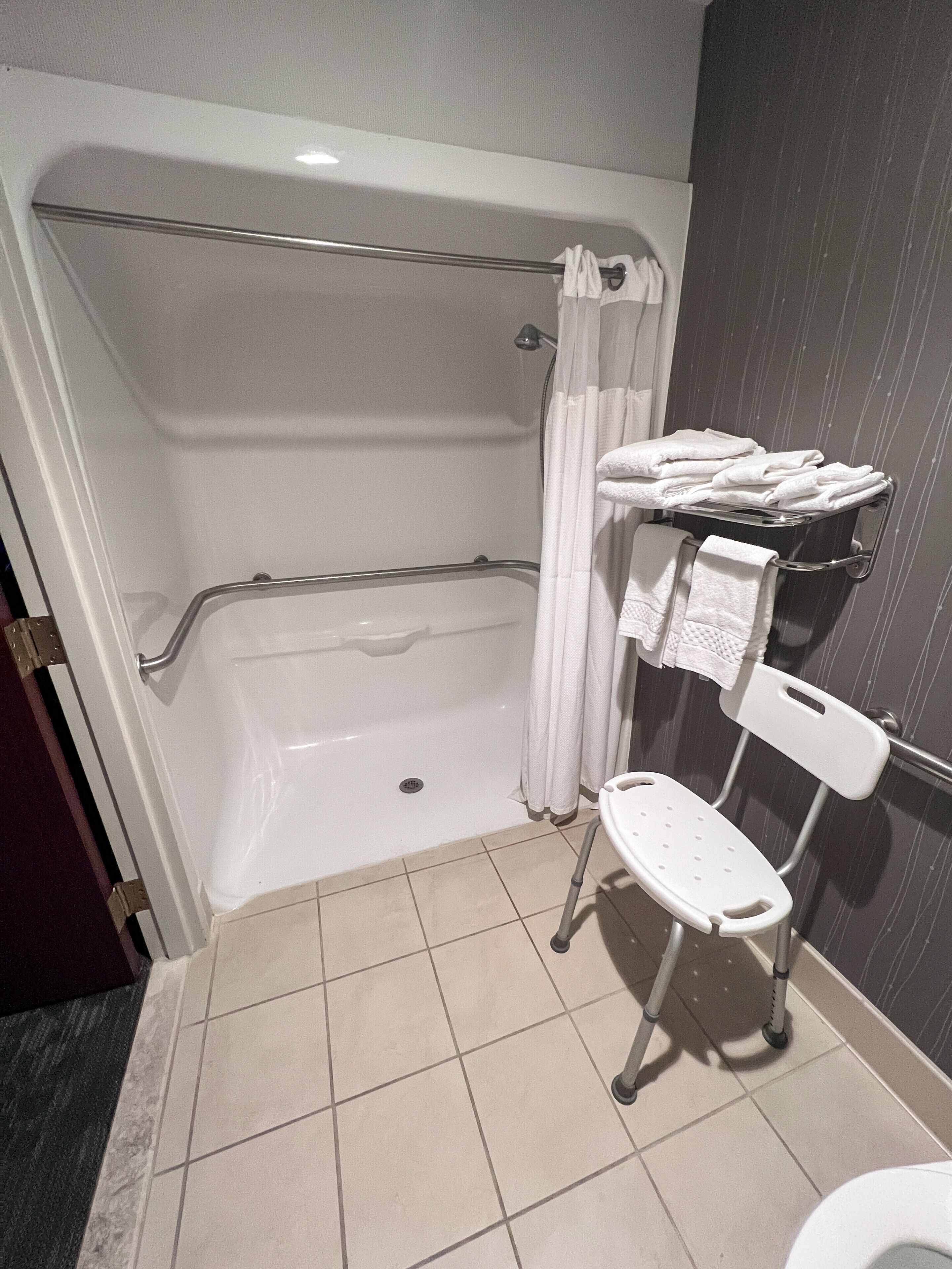 A bathroom with a bathtub, a shower curtain, a towel rack, and a wheelchair-accessible bench.