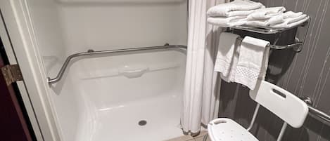A bathroom with a bathtub, a shower curtain, a towel rack, and a wheelchair-accessible bench.