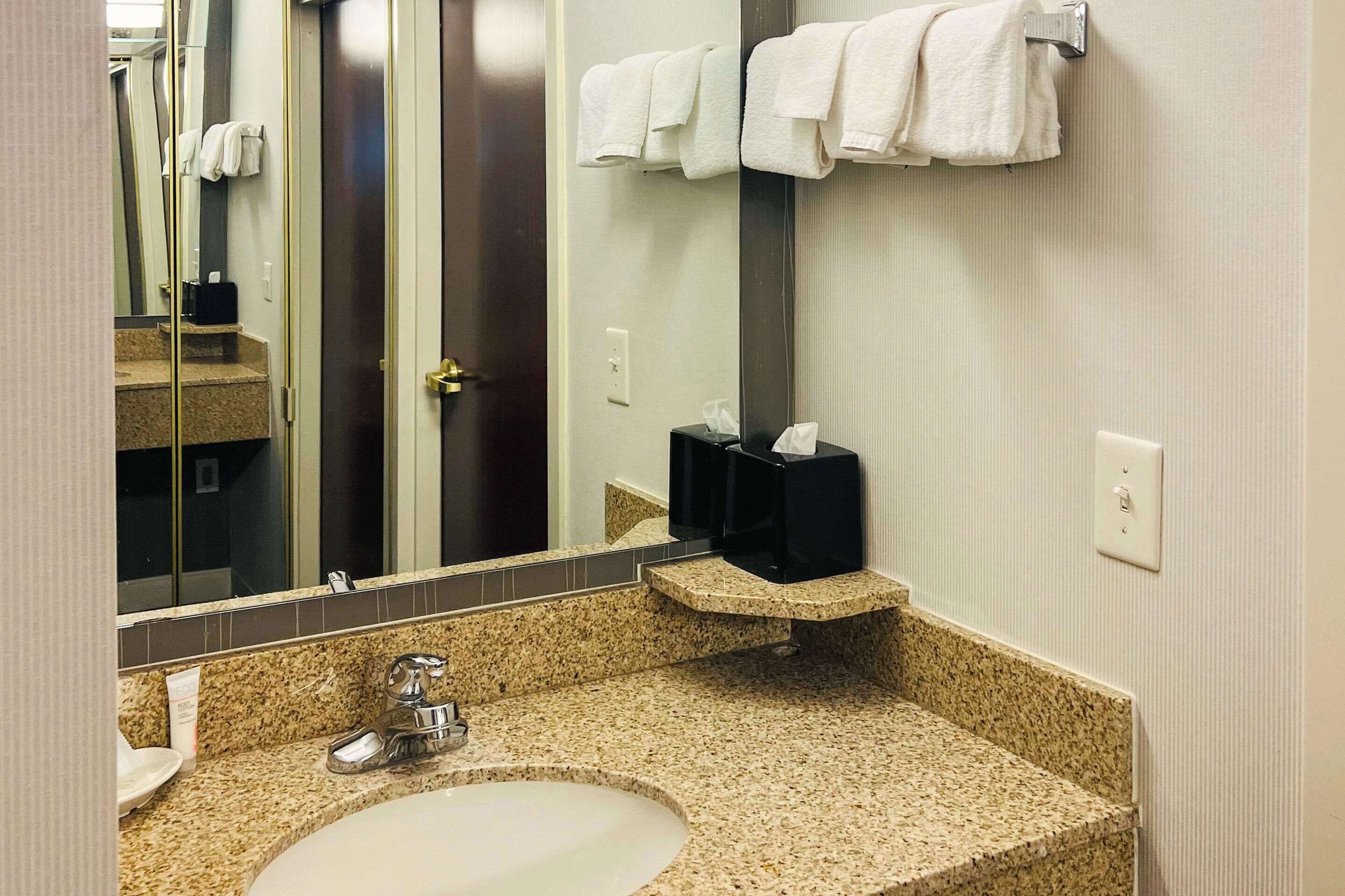 A bathroom with a granite countertop sink, a mirror, and a towel rack.