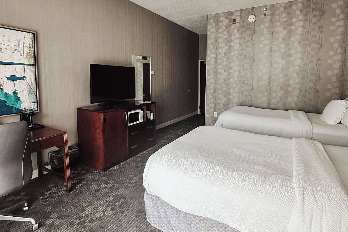 A hotel room with a large bed, a desk with a television, a dresser, and a microwave.