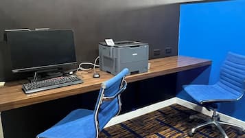 An office cubicle with a desk, computer, printer, and two blue chairs.