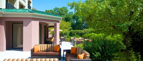 A hotel patio with outdoor seating, a covered area, and lush greenery.