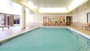 A swimming pool with a tiled deck, chairs, and a glass partition wall.