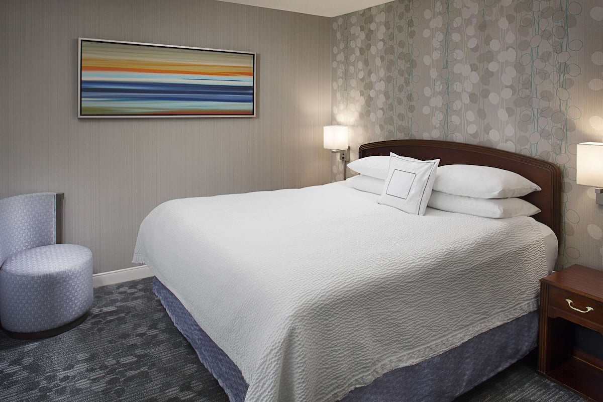 A hotel room with a large bed, two bedside lamps, a chair, and a painting on the wall.