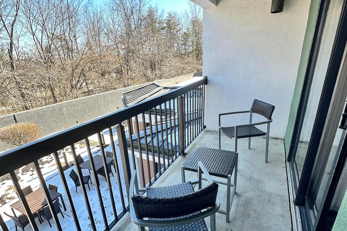 A balcony with a concrete floor, metal railing, and two wicker chairs.
