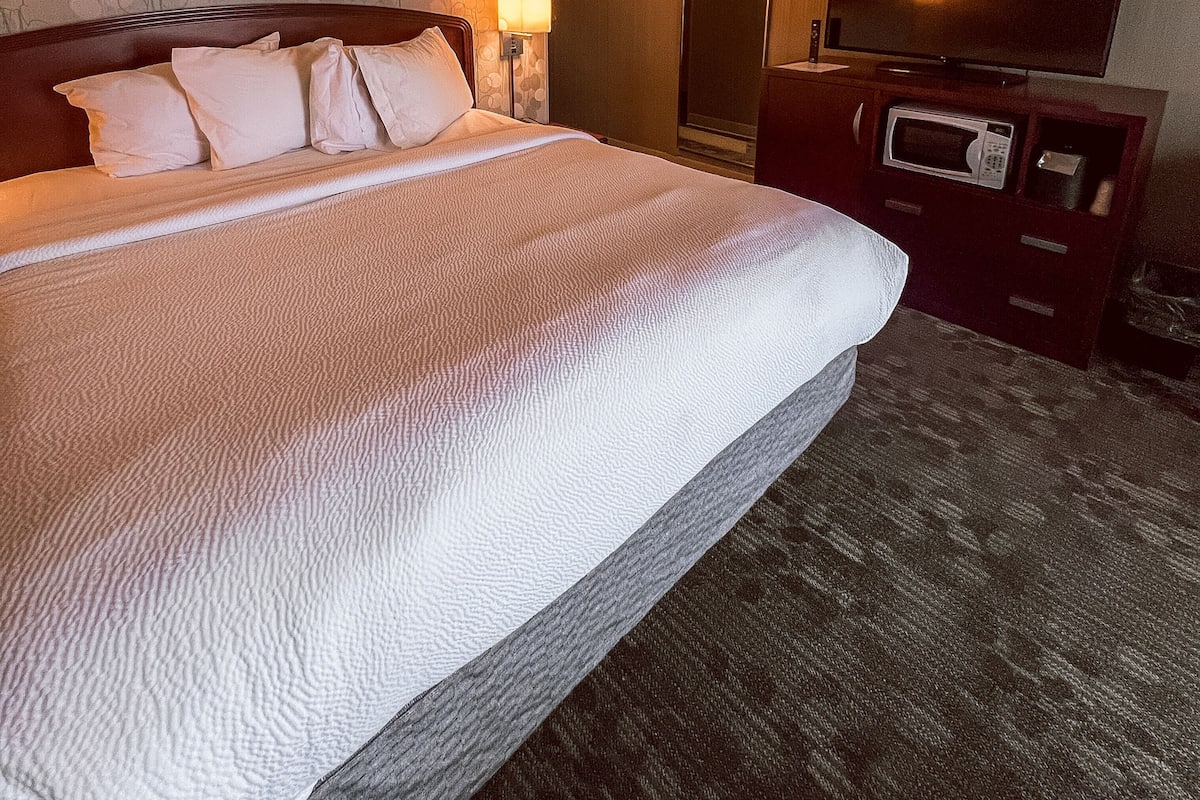 A hotel room with a large bed, a flat-screen TV, a microwave, and a dresser.